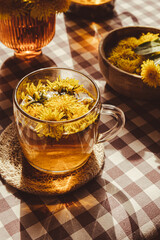 Dandelion flower healthy tea in glass teapot and glass cup on table. Delicious herbal tea from fresh dandelion flowers at home at summer day. Green clearing Hot dandelion tea in a glass teapot