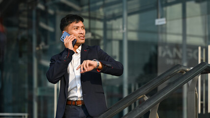 Busy young businessman in formal wear talking on mobile phone walking on city street, going to an important meeting