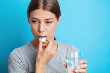Woman holding pill and glass water, taking medicine from headache, stomach pain or taking vitamins