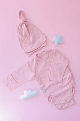 A pink suit for a newborn lies on a pink background. Cap and bodysuit. Clothes for newborns. Pregnancy. Waiting for the girl.