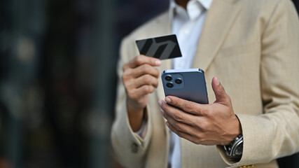 Modern businessman holds credit card and using smartphone. Banking, finance, online payment, e commerce