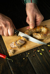 The hands of the cook with a knife cut grilled pork sausage on a cutting kitchen board for a delicious lunch. Northern Thailand national dish