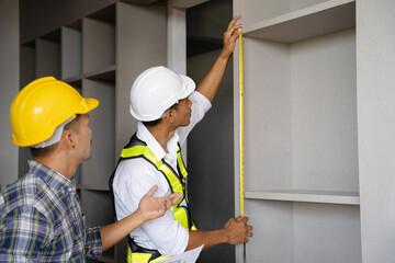 Male construction engineer or architect in hard hat using measure tape at the construction site.