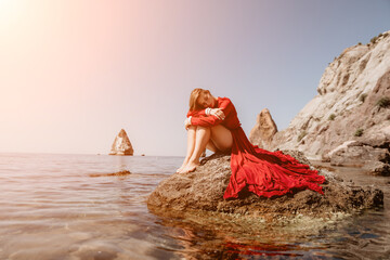 Woman travel sea. Happy tourist in red dress enjoy taking picture outdoors for memories. Woman traveler posing on the rock at sea bay surrounded by volcanic mountains, sharing travel adventure journey