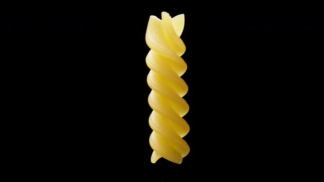 spiral pasta fusilli, one piece rotates on a black background and moves horizontally.