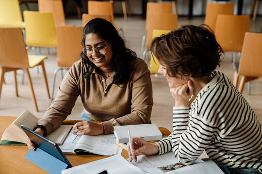 Two cheerful female students studying together in college library