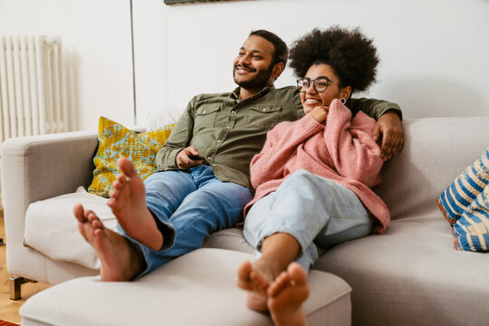 Cheerful couple watching tv together while sitting on couch