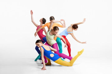 Group of artistic, young girls, ballerinas in multicolored clothes making performance, dancing against grey background. Concept of beauty, creativity, classic dance style, elegance, contemporary art