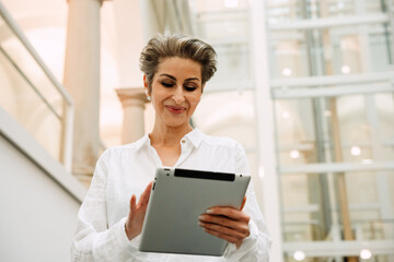 Portrait of cheerful woman art gallery manager using tablet while standing in museum