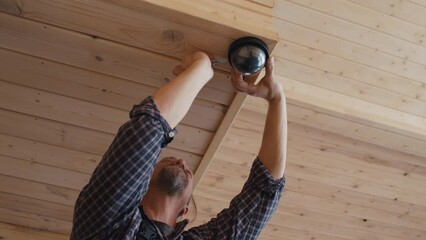 Low angle view shot of mature Caucasian handyman setting sensor under wooden staircase in modern house