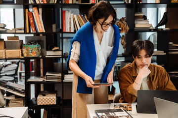 Mature woman and young man using laptop while working together in office
