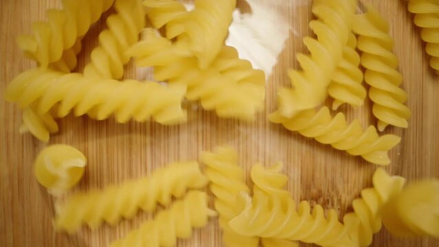 Fusilli pasta falls into a glass bowl on a wooden table, top view. Dolly slider extreme close-up. Slow motion
