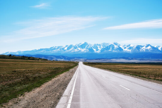 Straight forward asphalt road leads into the distance to the mountain range. Panoramic landscape image