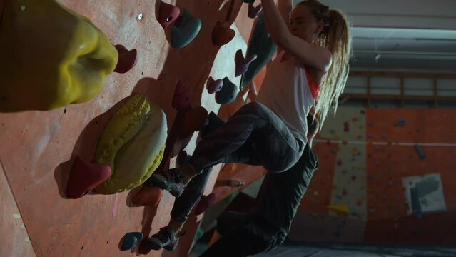 A beautiful cinematic shot with a pretty blonde woman with a beautiful hairstyle who is bouldering at the climbing wall and takes a beautiful pose on the wall. High quality 4k footage