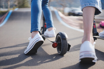 Teenager exploring pump track park with electric scooter at sunset. Woman's legs in sneakers pushing electric scooter. Girl riding on ecological and urban transportation.