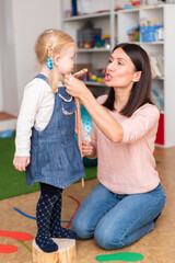 Woman speech therapist helps cute girl to learn correct pronunciation and literate speech