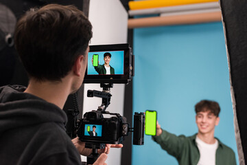 Professional photographer shooting a young man showing smartphone with green screen