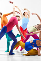Modern choreography. Group of young girls, ballet dancers in colorful clothes dancing against grey background. Cropped. Concept of beauty, creativity, classic dance style, elegance, contemporary art