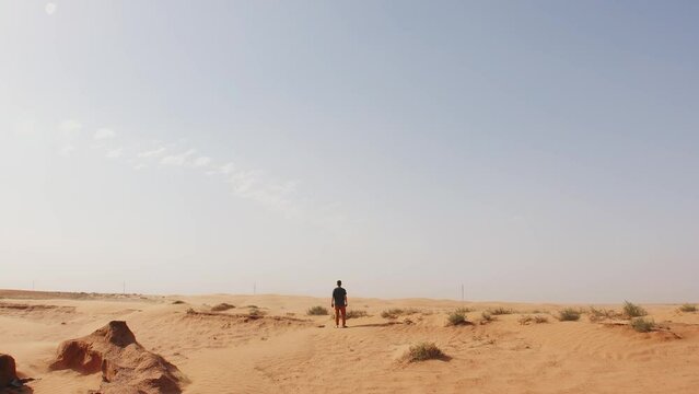 Young man goes through desert with clay stones and camel thorns. Concept of solitude and reflection. Slow motion