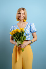 Beautiful young woman holding bunch of tulips and smiling against blue background