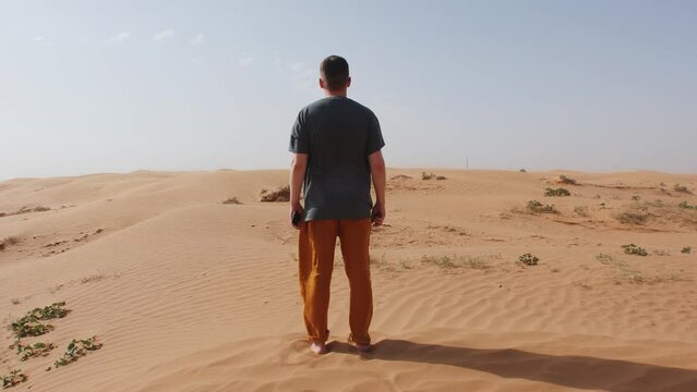 Man stands barefoot in desert on wind. Back view. Concept of solitude and contemplation. Slow motion