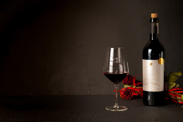 Glass red wine and 
a bottle of wine and rose on a black background. On black background.  Italian...