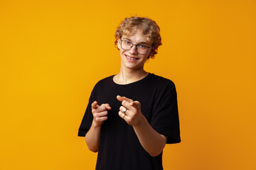 Fototapeta premium Young curly-haired man in glasses pointing to camera against yellow background
