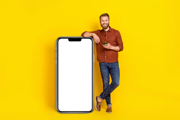 Full body photo of positive guy stand near huge empty space telephone isolated on yellow color background