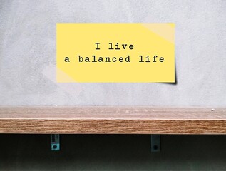 Note stick on wall over a shelf with text written I LIVE A BALANCED LIFE, positive mantra...