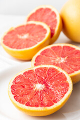 Fototapeta na wymiar Close-up of split red grapefruits on plate and white tablecloth, vertical