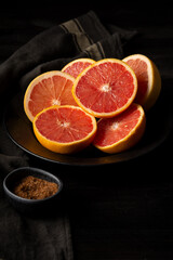 Top view of cut red grapefruits with brown sugar on plate and black cloth, vertical, with copy space