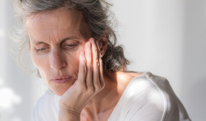 Fototapeta premium Closeup of middle aged woman with head in hands looking down with shadows in background (selective focus)