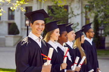 Happy graduate students dressed in black graduation gowns holding diplomas. Portrait of smiling diverse academy graduates in black mortar board caps celebrating graduation college or university