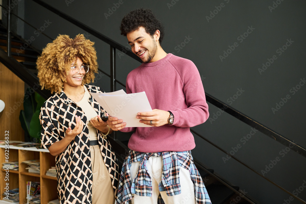 Aufkleber two young smiling economists in casualwear discussing financial papers with graphic data and analyzi