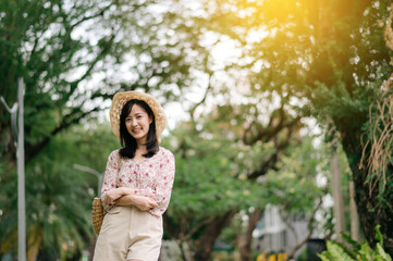 Fototapeta na wymiar Portrait of asian young woman traveler with weaving hat and basket happy smile on green public park nature background. Journey trip lifestyle, world travel explorer or Asia summer tourism concept.