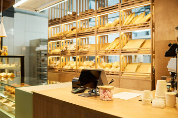 Workplace of baker or clerk of bakery shop or cafeteria with tablet, stacks of disposable paper cups and payment terminal on counter - obrazy, fototapety, plakaty