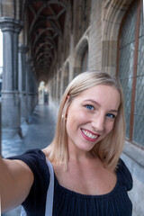 Naklejka na ściany i meble Selfie time, Attractive blonde young funky blogger is making photo for her social networks page. Young happy woman taking selfie in a European city. atmosphere and a beautiful smiling girl. High