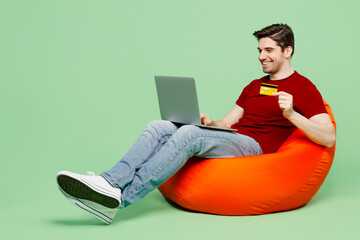 Full body young IT man wear red t-shirt casual clothes sit in bag chair using laptop pc computer...