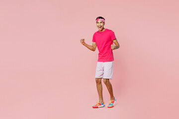 Full body young man of African American ethnicity he wear headscarf t-shirt casual clothes doing winner gesture celebrate clenching fists say yes isolated on pastel plain light pink color background. © ViDi Studio