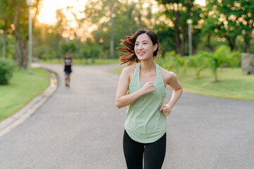 Fit Asian young woman jogging in park smiling happy running and enjoying a healthy outdoor lifestyle. Female jogger. Fitness runner girl in public park. healthy lifestyle and wellness being concept