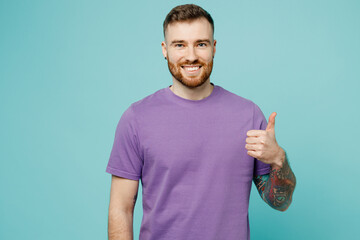 Young satisfied smiling happy fun cheerful man he wears purple t-shirt showing thumb up like...