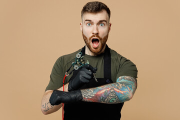 Surprised happy fun tattooer master artist tattooed man wear green t-shirt apron hold machine black...