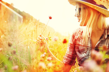 Woman picking flower in field with lens flare for freedom, wellness and fresh air in countryside. Nature, summer and hipster female person in natural meadow for relax, sustainability and ecology