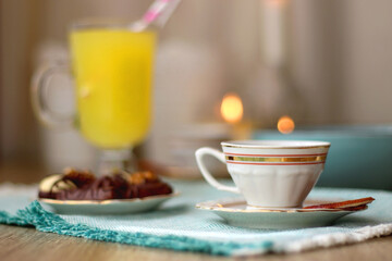 Plate of chocolate pralines, bowl of cookies, cups of tea, glasses of juice and lit candles on the table. Selective focus.