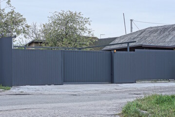 one black metal gate on an iron long fence wall on the street near a gray asphalt road