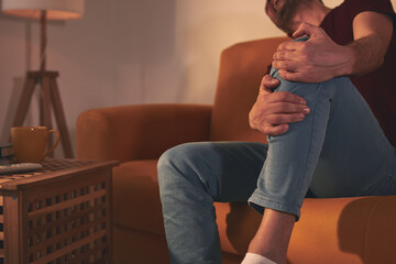 Man with knee pain sitting on a sofa at home.