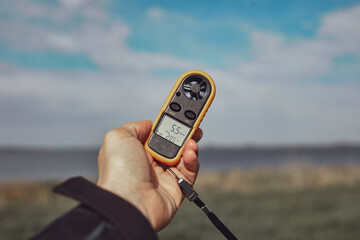 Person holding modern digital anemometer outdoors for measuring wind speed, temperature, humidity and other atmospheric effects. - obrazy, fototapety, plakaty