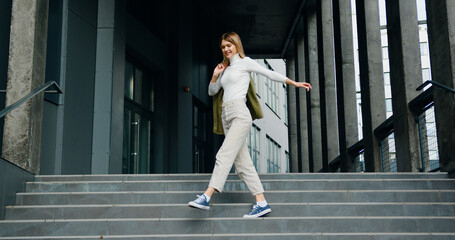 Beautiful smiling girl holding a jacket walks up the stairs and has fun dancing. Happy joyful lifestyle concept.