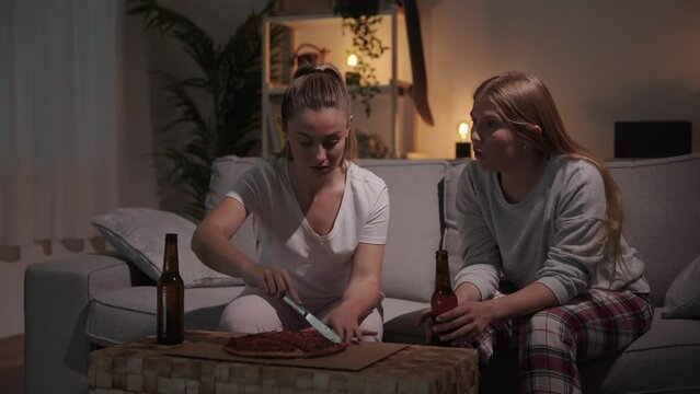 Young women wearing pyjamas eating pizza and talking.