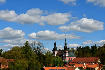 A view of an old church or monastery painted pink located next to some rural settlement and vast forest or moor seen from a hill on a sunny summer day on a Polish countryside during a hike - obrazy, fototapety, plakaty